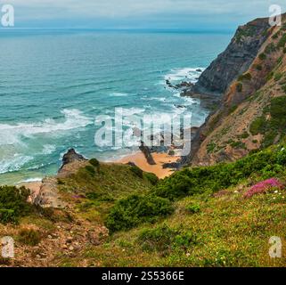 Sandstrand mit felsigen Bergrücken trübes Wetter Aussicht auf Sommer Atlantic an der felsigen Küste (Costa Vicentina, Algarve, Portugal). Und Ocean Surf Wellen. Stockfoto