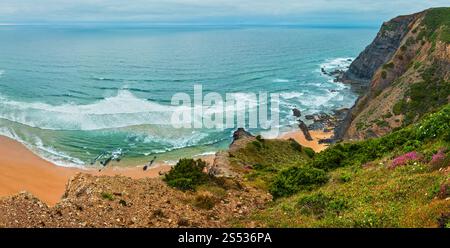 Sandstrand mit felsigen Bergrücken trübes Wetter Aussicht auf Sommer Atlantic an der felsigen Küste (Costa Vicentina, Algarve, Portugal). Und Ocean Surf Wellen. Stockfoto
