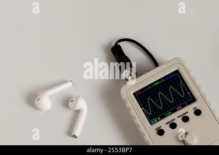 Kabellose Kopfhörer und Oszilloskop in Nahaufnahme auf hellem Hintergrund Stockfoto