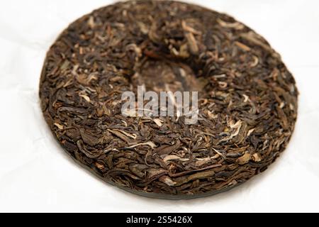 Gepresster roher pu-erh-Teekuchen mit natürlicher lockerer Blattstruktur und Details von gereiften Teeblättern, die die Tradition der Handwerkskunst in der Teezubereitung symbolisieren Stockfoto