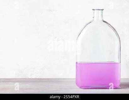 Glasflasche mit rosa Aquarelllösung auf grauem Holzbrett in der Nähe von grauer Betonwand Stockfoto