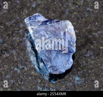 Nahaufnahme einer Probe von natürlichem Mineral aus der geologischen Sammlung - unpolierter Kordierit (Iolith) Kristall auf schwarzem Granit Hintergrund aus Madagaskar. Stockfoto