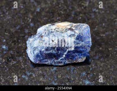 Nahaufnahme einer Probe von natürlichem Mineral aus geologischer Sammlung - rauer Kordierit (Iolith) Kristall auf schwarzem Granit Hintergrund aus Madagaskar. Stockfoto