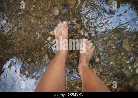 Die Textur des Bodens. Die Steine, die unter dem klaren Wasser sichtbar sind. Wasser kräuselt die Flussstrahlen auf den Felsen. Stockfoto