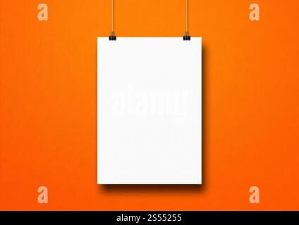 Weißes Poster hängt an einer orangen Wand mit Clips. Leere Modellvorlage. Weißes Poster hängt an einer orangen Wand mit Clips Stockfoto