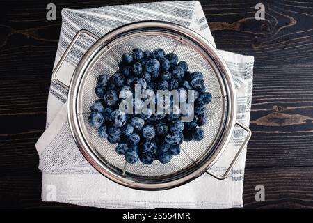 Frisch gewaschene Heidelbeeren im Mesh-Sieb: Feuchte Heidelbeeren mit Wassertropfen in einem Metallsieb, das auf einem Geschirrtuch abtropft Stockfoto