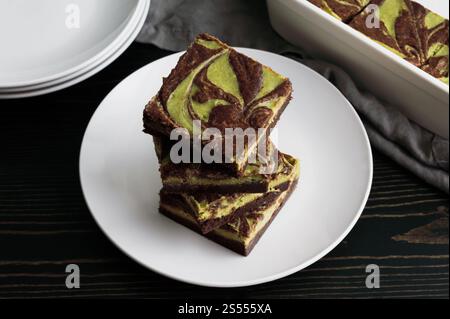 Matcha Cheesecake Brownies Angle View: Dunkle Schokoladen-Brownies mit grünem Tee, Frischkäse-Füllung, gestapelt auf weißem Dessertteller Stockfoto