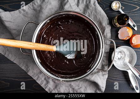 Brownie-Teig aus geschmolzener dunkler Schokolade in einem Topf: Brownie-Teig gemischt mit Silikonspachtel in einem kleinen Topf mit Zutaten an der Seite Stockfoto