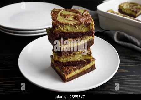Matcha Cheesecake Brownies Angle View: Dunkle Schokoladen-Brownies mit grünem Tee, Frischkäse-Füllung, gestapelt auf weißem Dessertteller Stockfoto