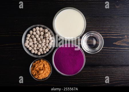 Violette Süßkartoffel-Bubble-Tee-Zutaten: Süßkartoffeln in Pulverform, Tapioka-Kugeln und weitere Zutaten auf einem dunklen Holztisch Stockfoto