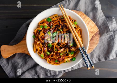 Schalotten Chili Oil Nudeln serviert in einer Ramen Bowl: Heiße und scharfe Lo meine Nudeln garniert mit Chili Crisp und Zwiebeln serviert mit Essstäbchen Stockfoto