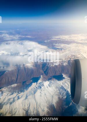 Blick vom Bullauge des Flugzeugs auf den Motor und die mit Schnee bedeckten Gipfel. Blick vom Bullauge des Flugzeugs auf den Motor und die Bergspitzen mit bedeckt Stockfoto