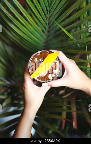 Orange Americano Iced Coffee in der Hand halten. Eisschwarzer Kaffee gemischt mit Orangensaft Stockfoto