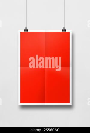 Rotes gefaltetes Poster, das an einer weißen Wand mit Clips hängt. Leere Modellvorlage. Rotes gefaltetes Poster, das an einer weißen Wand mit Clips hängt Stockfoto