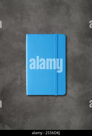 Blaues geschlossenes Notizbuchmodell isoliert auf dunklem Betonhintergrund. Blaues geschlossenes Notizbuch auf dunklem Betonhintergrund Stockfoto
