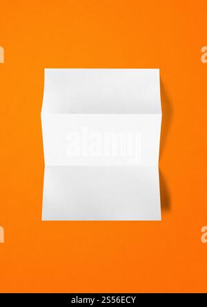 Leeres gefaltetes weißes A4-Papierblattmodell isoliert auf orangem Hintergrund. Leere gefaltete weiße A4-Papiervorlage auf orangem Blatt Stockfoto