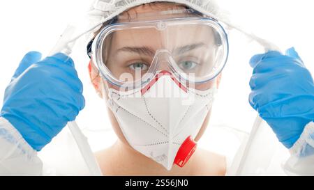 Erschöpfter und müder Arzt, der in die Kamera schaut, nachdem er Schutzanzug, Schutzbrille und Gesichtsmaske ausgezogen hat. Mediziner kämpfen gegen Stockfoto
