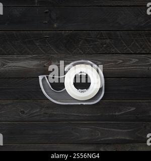 Transparenter Abroller mit Scotch-Klebeband isoliert auf schwarzem Holzhintergrund. Scotch Tape Spender isoliert auf schwarzem Holzhintergrund Stockfoto