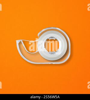 Transparenter Abroller mit Scotch-Klebeband, isoliert auf orangem Hintergrund. Scotch Tape Spender isoliert auf orangem Hintergrund Stockfoto