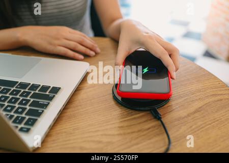 Laden des Mobiltelefonakkus mit dem drahtlosen Gerät in der Tabelle. Smartphone wird auf einem Ladepad aufgeladen. Mobiltelefon in der Nähe des kabellosen Ladegeräts Stockfoto