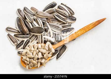 Draufsicht auf Kerne in Holzlöffel und Stapel Sonnenblumenkerne auf grauer Keramikplatte Stockfoto