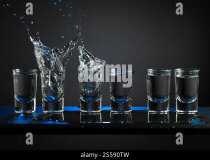 Alkoholische Schüsse von Wodka oder starkes Getränk in kleinen Gläsern. Ein Stück Eis fällt in eine Gläser, was einen Spritzer erzeugt. Kopierbereich. Stockfoto
