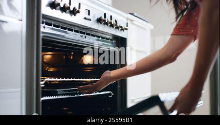 Frau, Hände und Ofen in der Küche zum Backen, Rezeptprozess und Tablett auf dem Regal zu Hause. Weibliche Person, elektrische Ausrüstung und Kochen am Herd zum Essen Stockfoto
