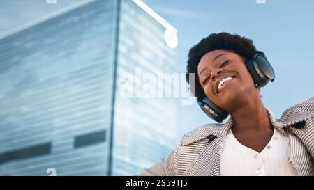 Junge Frau genießt tagsüber Musik mit Kopfhörern in einer urbanen Umgebung Stockfoto