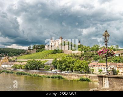 Ein malerischer Blick auf ein historisches Schloss auf einem Hügel, umgeben von üppigem Grün, mit einer Stadt am Fluss und einer Straßenlaterne im Vordergrund Stockfoto