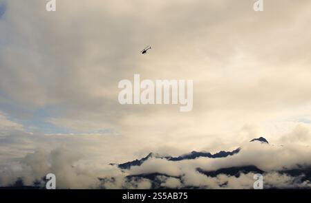 Ein Hubschrauber fliegt durch die dichte Wolkendecke über die Berge im dichten Nebel in Alaska, USA. Stockfoto