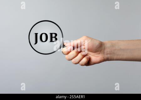 Konzept der Jobsuche. Frau, die durch eine Lupe auf grauem Hintergrund ein Wort ansieht, Nahaufnahme Stockfoto