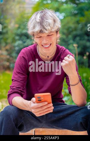 Glücklicher Junger Mann, Der Erfolg Feiert, Während Er Das Smartphone Im Freien Nutzt. Vertikal Stockfoto