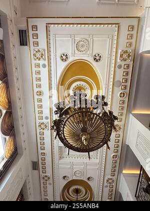 Atemberaubende Aussicht auf einen großen Kronleuchter, der von einer reich verzierten Decke in einem historischen Gebäude hängt. Komplizierte Details und goldene Akzente sorgen für einen Stockfoto