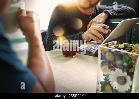 Kaffeepause im Büro mit zwei Designerkollegen, die bei einer Tasse Kaffee, einer Blumenvase und einer intelligenten Tastatur auf Marmor sitzen Stockfoto