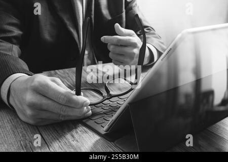 Erfolg Geschäftsmann Hand mit Brillen, digital-Tablette Docking-smart-Tastatur auf Holz Schreibtisch, schwarz weiß Stockfoto