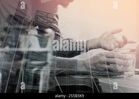 Doppelbelichtung des Website-Designers Hand hält Glas des Wassers, digitales Tablet und Computer-Laptop auf Holzschreibtisch, Londoner Architektur Stockfoto