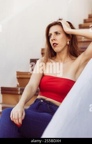 Eine Frau in einem roten Dach sitzt auf einer Treppe und hat einen nachdenklichen Ausdruck, Foto mit Kopierraum. Stockfoto