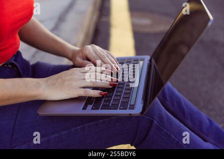 Nahaufnahme einer Frau, die auf dem Boden sitzt und auf einem Laptop tippt. Stockfoto