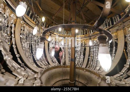 Jason Cardwell vom Tower Ballroom Team inspiziert das Innere eines 1-Tonnen-Kronleuchters, der von der Decke in ein speziell gefertigtes Gerüst abgesenkt wurde, bevor die beiden weltberühmten Kronleuchter im Blackpool Tower in Lancashire jährlich gereinigt und restauriert werden. Während die beiden Kronleuchter abgesenkt werden, wird ihr einzigartiger Seilmechanismus - der weltweit einzige seiner Art - zum ersten Mal in der Geschichte der Ballsäle ersetzt, ein Projekt, das in den nächsten Wochen abgeschlossen wird. Bilddatum: Dienstag, 14. Januar 2025. Stockfoto