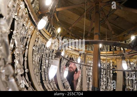 Jason Cardwell vom Tower Ballroom Team inspiziert das Innere eines 1-Tonnen-Kronleuchters, der von der Decke in ein speziell gefertigtes Gerüst abgesenkt wurde, bevor die beiden weltberühmten Kronleuchter im Blackpool Tower in Lancashire jährlich gereinigt und restauriert werden. Während die beiden Kronleuchter abgesenkt werden, wird ihr einzigartiger Seilmechanismus - der weltweit einzige seiner Art - zum ersten Mal in der Geschichte der Ballsäle ersetzt, ein Projekt, das in den nächsten Wochen abgeschlossen wird. Bilddatum: Dienstag, 14. Januar 2025. Stockfoto
