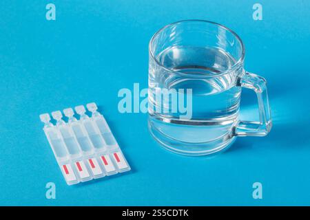 Eine Tasse Wasser und Röhrchen mit einer neuen Generation von Metabiotika auf blauem Hintergrund. Darmbehandlung, Wiederherstellung der Mikroflora nach Dysbacter Stockfoto