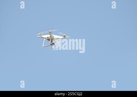 Große weiße Drohne, die in einem hellen wolkenlosen blauen Himmel schwebt, Funksteuerhubschrauber mit tragbarer Videokamera-Versorgung. Große weiße Drohne, die in A schwebt Stockfoto