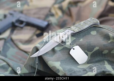 Army Dog Tag Token mit Messer und Pistole liegen auf gefaltetem grünen Stoff. Ein Set von Militärveteranen oder ein altes Trophäenkit. Army Dog Tag Stockfoto