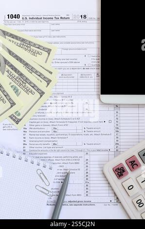 Zusammensetzung der Gegenstände, die auf dem Steuerformular 1040 liegen. Dollarscheine, Stift, Rechner, Smartphone, Büroklammer und Notizblock. Die Zeit, Steuern zu zahlen Stockfoto