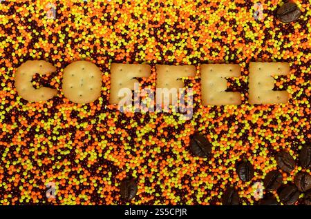 Kaffee. Das Wort aus den eßbaren Cracker-Buchstaben liegt auf dem glasierten Pulver. Eine große Anzahl süßer, farbenfroher Perlen von sehr kleiner Größe zur Dekoration Stockfoto