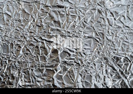 Dünnes, zerknittertes Blech aus zerkleinerter Aluminiumfolie mit glänzender, zerknitterter Oberfläche für Textur Stockfoto
