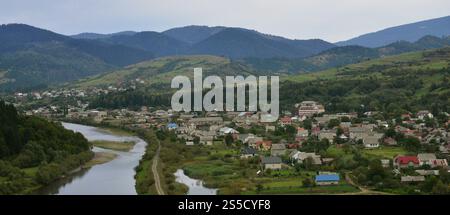 Eine wunderschöne Aussicht auf das Dorf Mezhgorye, Karpaten Region. Eine Menge von Wohngebäuden durch hohe Wald Berge und lange Fluss umgeben Stockfoto