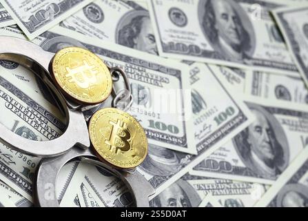 Polizeihandschellen und Bitcoins liegen auf einer großen Anzahl von Dollarscheine. Das Konzept der rechtlichen Probleme beim illegalen Kryptowährungsbergbau Stockfoto
