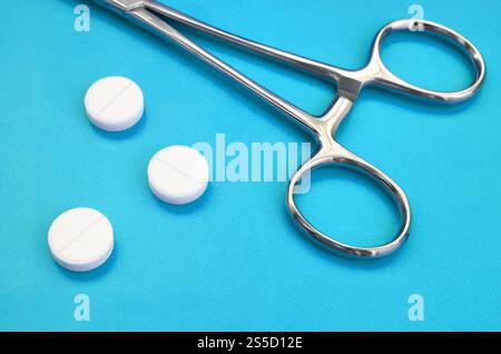 Mehrere weiße Tabletten und eine medizinische Schelle liegen auf einem hellblauen Hintergrund Oberfläche. Hintergrundbild über medizinische und pharmazeutische Themen Stockfoto