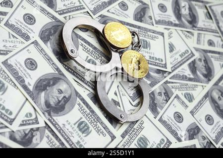 Polizeihandschellen und Bitcoins liegen auf einer großen Anzahl von Dollarscheine. Das Konzept der rechtlichen Probleme beim illegalen Kryptowährungsbergbau Stockfoto